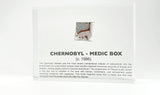 Clear acrylic display case featuring a historical fragment of a Chernobyl medic box, offering an educational presentation for collectors and those interested in nuclear history.