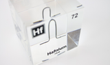 Clear acrylic cube displaying a Hafnium element (Atomic Number 72) embedded within, offering a scientific presentation for collectors and science enthusiasts.