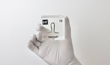 Clear acrylic cube displaying a Hafnium element (Atomic Number 72) embedded within, offering a scientific presentation for collectors and science enthusiasts.