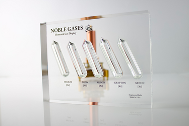 Close-up of a noble gas display made of acrylic. The display features several sections, each containing a different noble gas in its inert, gaseous form, with clear labels identifying each gas.