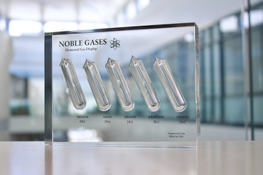 Close-up of a noble gas display made of acrylic. The display features several sections, each containing a different noble gas in its inert, gaseous form, with clear labels identifying each gas.