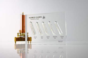 Close-up of a noble gas display made of acrylic. The display features several sections, each containing a different noble gas in its inert, gaseous form, with clear labels identifying each gas.