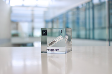 Clear acrylic cube displaying a Potassium element (Atomic Number 19) embedded within, offering a scientific presentation for collectors and science enthusiasts.
