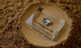 Close-up piece of SR-71 Blackbird titanium embedded in clear acrylic. The fragment is metallic and jagged, which highlights its history from the high-speed reconnaissance aircraft.