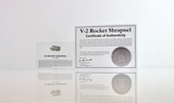 Close-up piece of V-2 rocket shrapnel embedded in clear acrylic. The fragment is metallic and jagged, with a distinctive shape that highlights its history from World War II rocket warfare.