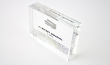 Close-up piece of V-2 rocket shrapnel embedded in clear acrylic. The fragment is metallic and jagged, with a distinctive shape that highlights its history from World War II rocket warfare.