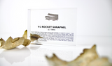 Close-up piece of V-2 rocket shrapnel embedded in clear acrylic. The fragment is metallic and jagged, with a distinctive shape that highlights its history from World War II rocket warfare.