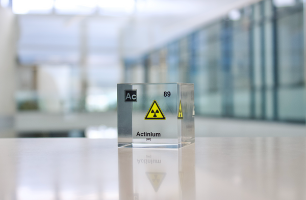 Clear acrylic cube with a suspended actinium (Ac) symbol and radioactive warning sign inside. The cube prominently displays actinium's atomic number 89, highlighting its scientific and radioactive properties in a modern, visually striking format.