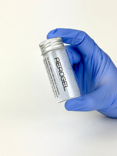 Hand wearing a blue glove holding a silver canister labeled 'Aerogel' on a white background