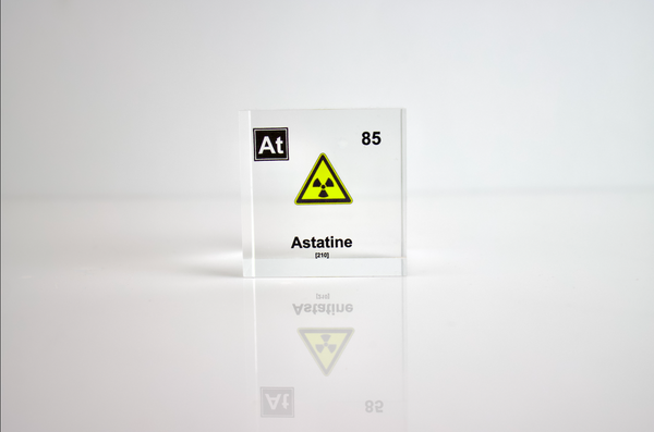 Clear acrylic cube displaying an Astatine element (Atomic Number 85) embedded within, offering a scientific presentation for collectors and science enthusiasts. Radiation symbol.