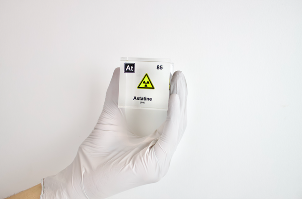 Clear acrylic cube displaying an Astatine element (Atomic Number 85) embedded within, offering a scientific presentation for collectors and science enthusiasts. Radiation symbol.