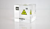 Clear acrylic cube displaying an Astatine element (Atomic Number 85) embedded within, offering a scientific presentation for collectors and science enthusiasts. Radiation symbol.