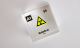 Clear acrylic cube displaying an Astatine element (Atomic Number 85) embedded within, offering a scientific presentation for collectors and science enthusiasts. Radiation symbol.