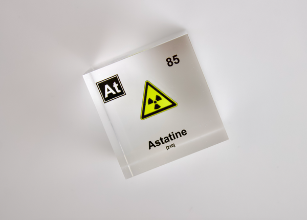 Clear acrylic cube displaying an Astatine element (Atomic Number 85) embedded within, offering a scientific presentation for collectors and science enthusiasts. Radiation symbol.