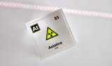 Clear acrylic cube displaying an Astatine element (Atomic Number 85) embedded within, offering a scientific presentation for collectors and science enthusiasts. Radiation symbol.
