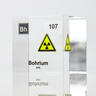 Clear acrylic cube displaying a Bohrium element (Atomic Number 107) embedded within, offering a scientific presentation for collectors and science enthusiasts. Radiation symbol.