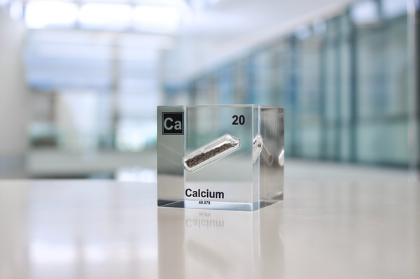 Clear acrylic cube displaying a Calcium element (Atomic Number 20) embedded within, offering a scientific presentation for collectors and science enthusiasts.