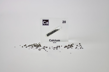 Clear acrylic cube displaying a Calcium element (Atomic Number 20) embedded within, offering a scientific presentation for collectors and science enthusiasts.