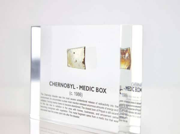 Clear acrylic display case featuring a historical fragment of a Chernobyl medic box, offering an educational presentation for collectors and those interested in nuclear history.