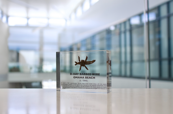 Clear acrylic display case featuring a historical fragment of D-Day barbed wire, offering an educational presentation for collectors and those interested in World War II history.