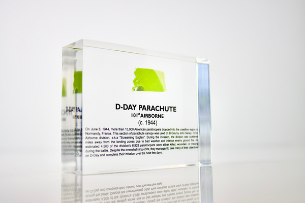 Clear acrylic display case featuring a historical fragment of a D-Day parachute, offering an educational presentation for collectors and those interested in World War II history.