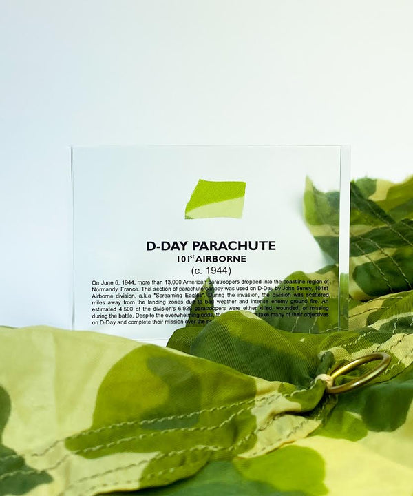 Clear acrylic display case featuring a historical fragment of a D-Day parachute, offering an educational presentation for collectors and those interested in World War II history.