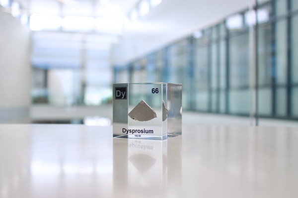 Clear acrylic cube displaying a Dysprosium element (Atomic Number 66) embedded within, offering a scientific presentation for collectors and science enthusiasts.