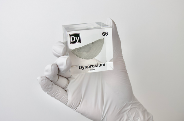 Clear acrylic cube displaying a Dysprosium element (Atomic Number 66) embedded within, offering a scientific presentation for collectors and science enthusiasts.