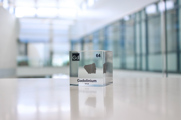 Clear acrylic cube displaying a Gadolinium element (Atomic Number 64) embedded within, offering a scientific presentation for collectors and science enthusiasts.