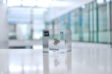 Clear acrylic cube displaying a Hafnium element (Atomic Number 72) embedded within, offering a scientific presentation for collectors and science enthusiasts.