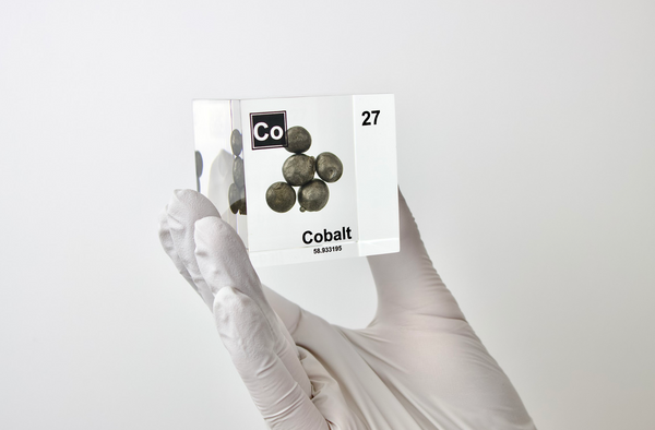 A hand holds cobalt element, Atomic Number 27, in a clear acrylic cube, displaying its name, atomic number, and key properties as shown on the periodic table. An educational and informative piece ideal for science enthusiasts and collectors.