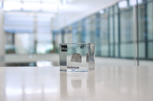 Clear acrylic cube displaying a Holmium element (Atomic Number 67) embedded within, offering a scientific presentation for collectors and science enthusiasts.