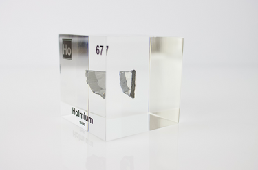 Clear acrylic cube displaying a Holmium element (Atomic Number 67) embedded within, offering a scientific presentation for collectors and science enthusiasts.