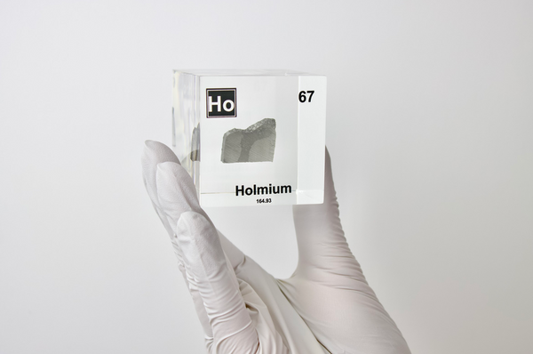 Clear acrylic cube displaying a Holmium element (Atomic Number 67) embedded within, offering a scientific presentation for collectors and science enthusiasts.