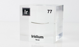Close-up of a piece of thin iridium element encased in a clear acrylic cube, showcasing its metallic luster and unique structure against the white background.