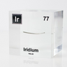 Close-up of a piece of thin iridium element encased in a clear acrylic cube, showcasing its metallic luster and unique structure against the white background.