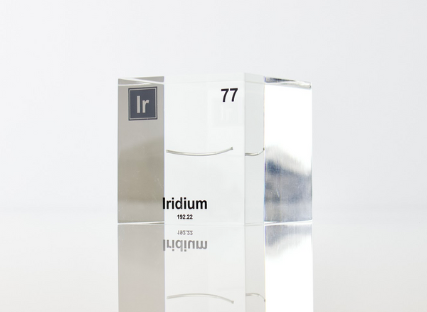 Close-up of a piece of iridium element encased in a clear acrylic cube, showcasing its metallic luster and unique structure against the white background.