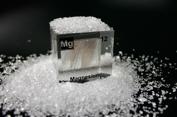 Clear acrylic cube featuring a Magnesium ampule with its atomic number 12. Epsom salts surrounding as Magnesium element is used for them. Ideal for educational displays, scientific collections, or as a distinctive decorative item.