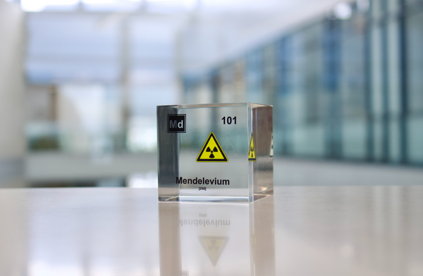 Clear acrylic cube displaying a Mendelevium element (Atomic Number 101) embedded within, offering a scientific presentation for collectors and science enthusiasts.