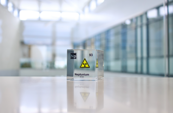 Clear acrylic cube displaying a Neptunium element (Atomic Number 93) embedded within, offering a scientific presentation for collectors and science enthusiasts.