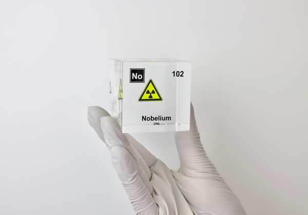 Clear acrylic cube displaying a Nobelium element (Atomic Number 102) embedded within, offering a scientific presentation for collectors and science enthusiasts.