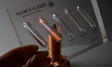 Close-up of a noble gas display made of acrylic. The display features several sections, each containing a different noble gas in its inert, gaseous form, with clear labels identifying each gas. 