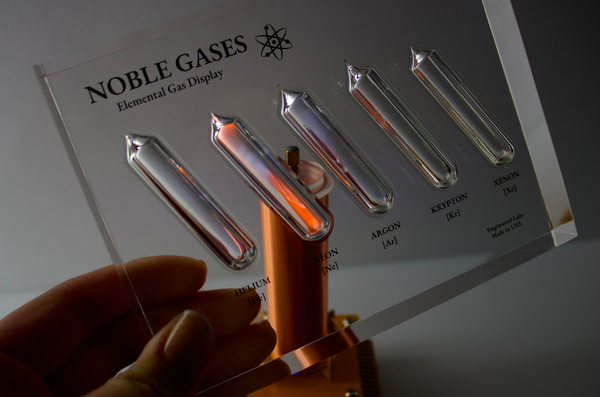 Close-up of a noble gas display made of acrylic. The display features several sections, each containing a different noble gas in its inert, gaseous form, with clear labels identifying each gas. 