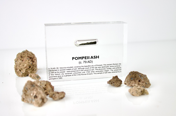 Close-up of ash from Pompeii, contained in a glass ampule and embedded in clear acrylic. The ash is fine and grayish, offering a tangible link to the historic eruption of Mount Vesuvius and the ancient city of Pompeii.