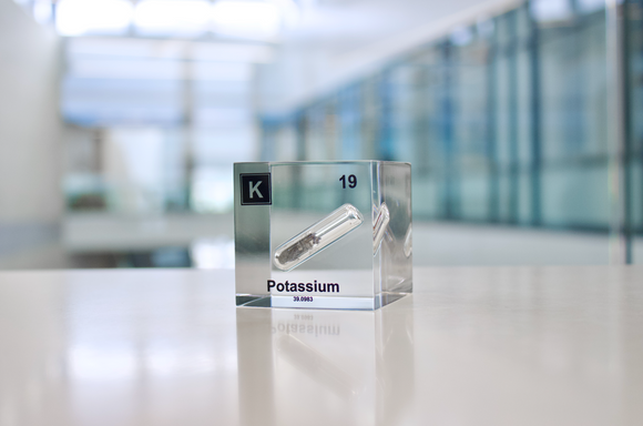 Clear acrylic cube displaying a Potassium element (Atomic Number 19) embedded within, offering a scientific presentation for collectors and science enthusiasts.