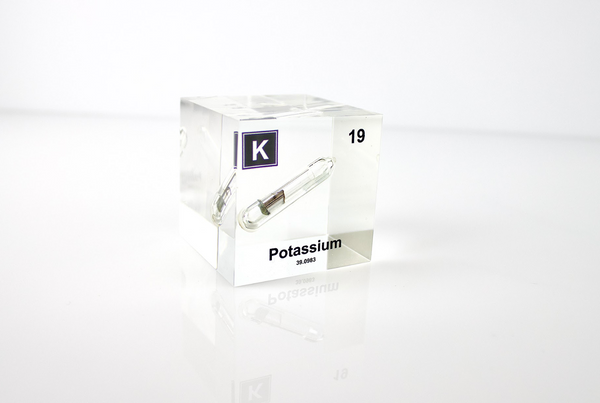 Clear acrylic cube displaying a Potassium element (Atomic Number 19) embedded within, offering a scientific presentation for collectors and science enthusiasts.