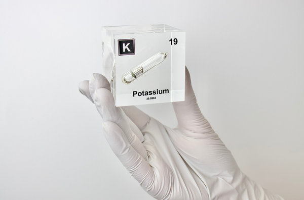 Clear acrylic cube displaying a Potassium element (Atomic Number 19) embedded within, offering a scientific presentation for collectors and science enthusiasts.