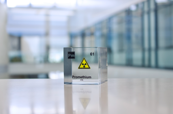 Clear acrylic cube displaying a Promethium element (Atomic Number 61) embedded within, offering a scientific presentation for collectors and science enthusiasts.