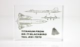 Close-up piece of SR-71 Blackbird titanium embedded in clear acrylic. The fragment is metallic and jagged, which highlights its history from the high-speed reconnaissance aircraft. A blueprint of the SR-71 aircraft is visible in the display.