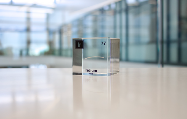 Close-up of a piece of iridium element encased in a clear acrylic cube, showcasing its metallic luster and unique structure.